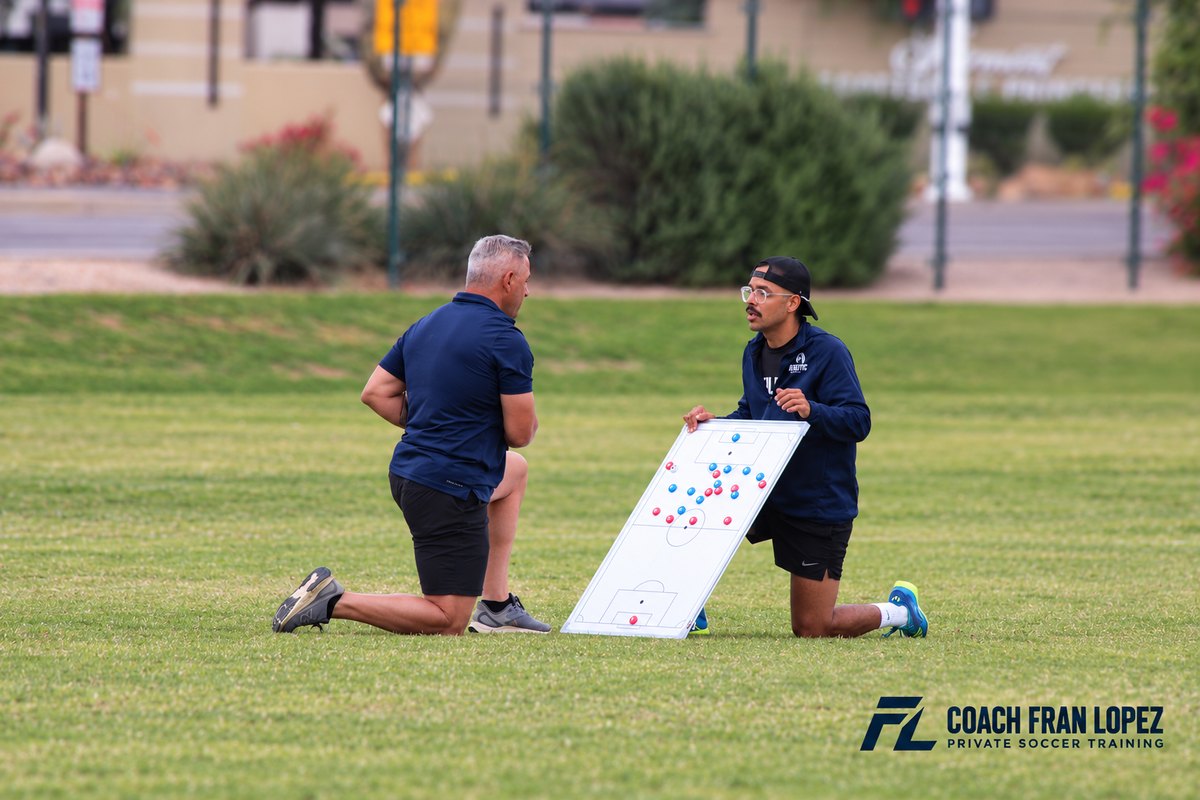 Coach Fran Lopez discussing soccer positioning with another coach using a tactics board
